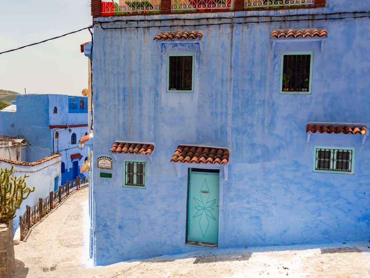 The blue-painted corner of a house in Chefchaouen's medina, with shuttered windows and a decorated door